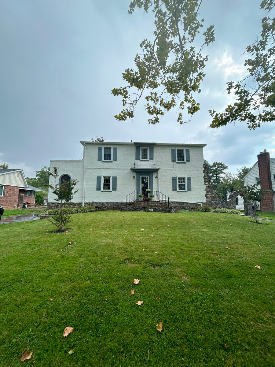 Two-story house with green shutters on a grassy lawn under a cloudy sky.