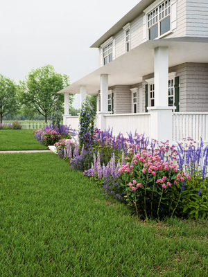 White house with a well-maintained lawn and flower bed cottage garden in front

