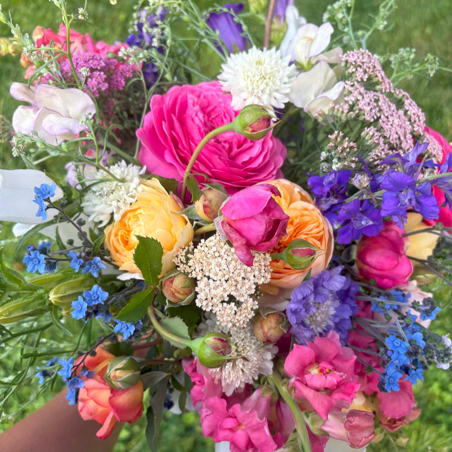 Bouquet of roses, snapdragons, yarrow, larkspur, scabiosa in pink, apricot, white, blue, and purple.